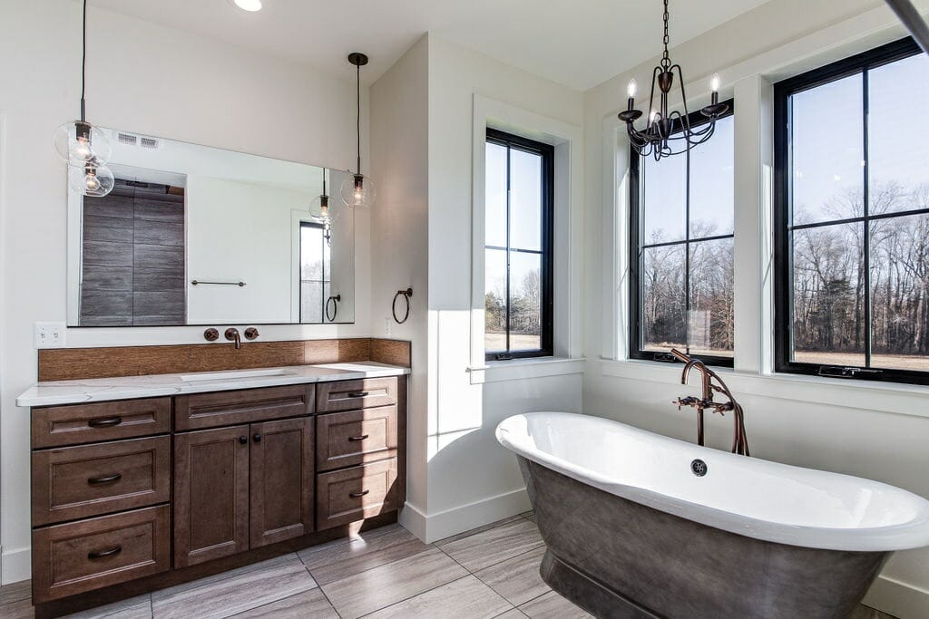 Rustic Meets Contemporary Style Bathroom Renovation - Golden Rule Builders - Bathroom remodel / renovation, large bathtub with a chandelier above, next to windows overlooking a beautiful view and receiving lots of natural light, and a large variety